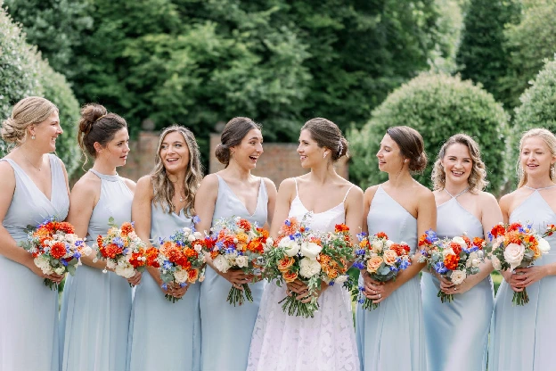 Bridesmaids in pale blue holding bright wedding bouquets by So Blooming Beautiful