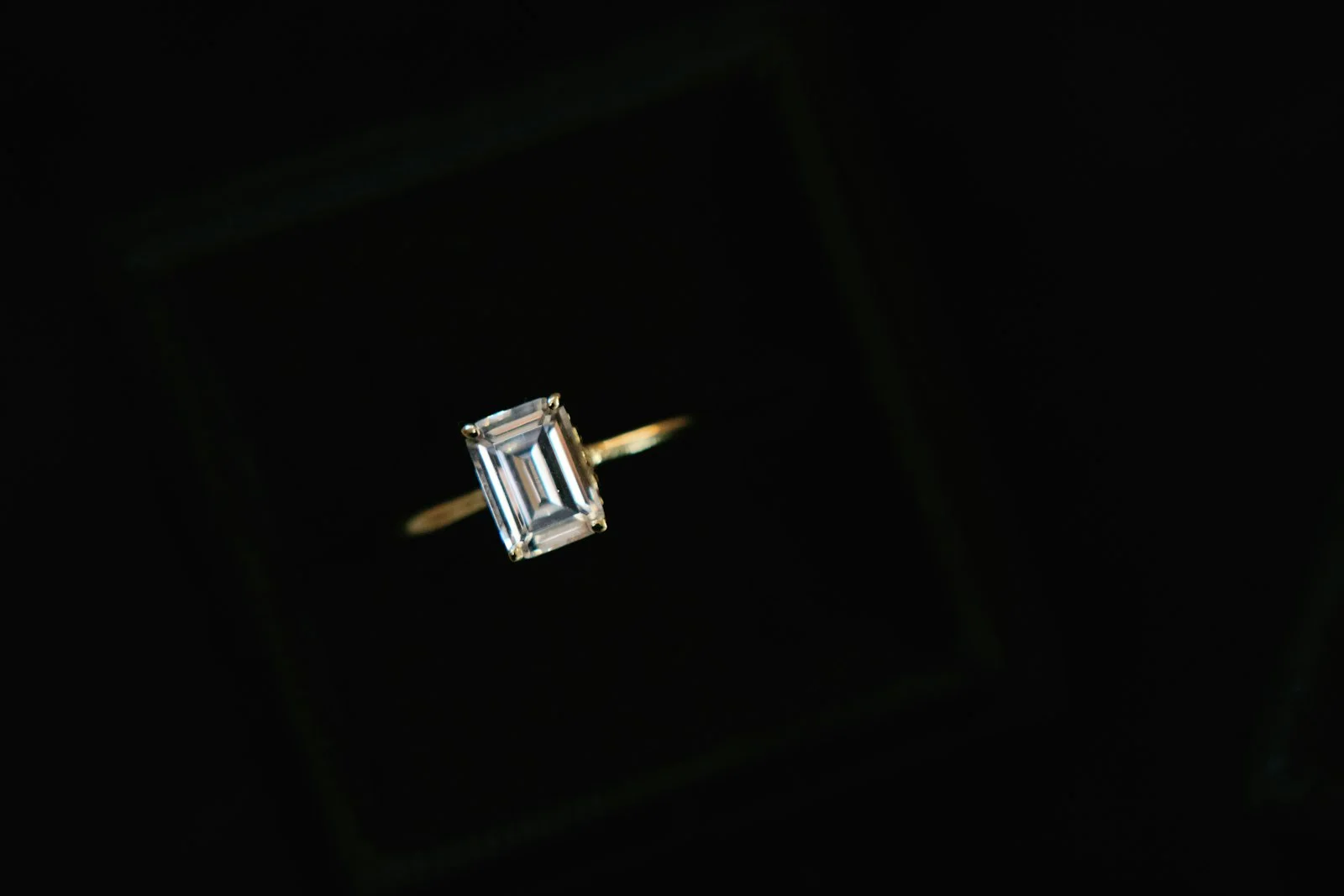 Emerald-cut solitaire diamond ring on a black background