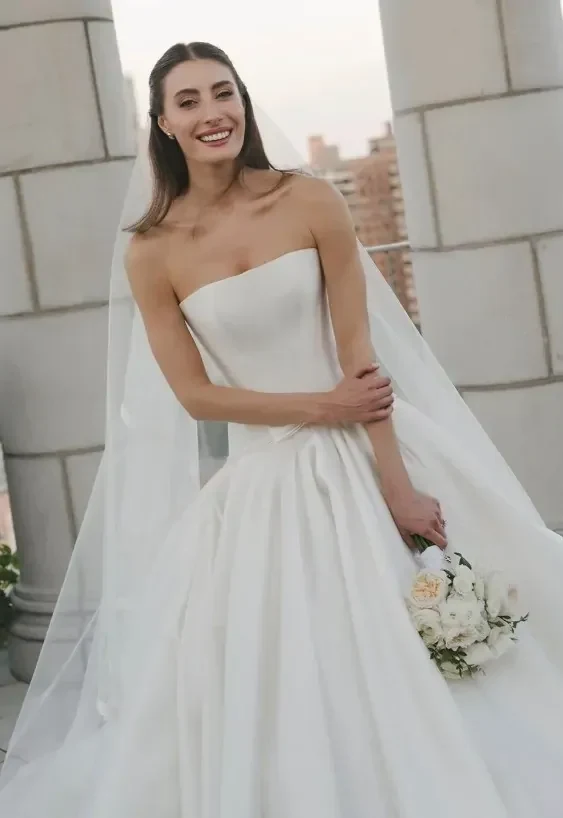 Bec Harding in a strapless white satin gown with a long veil and a bouquet of white roses | Wedded Wonderland