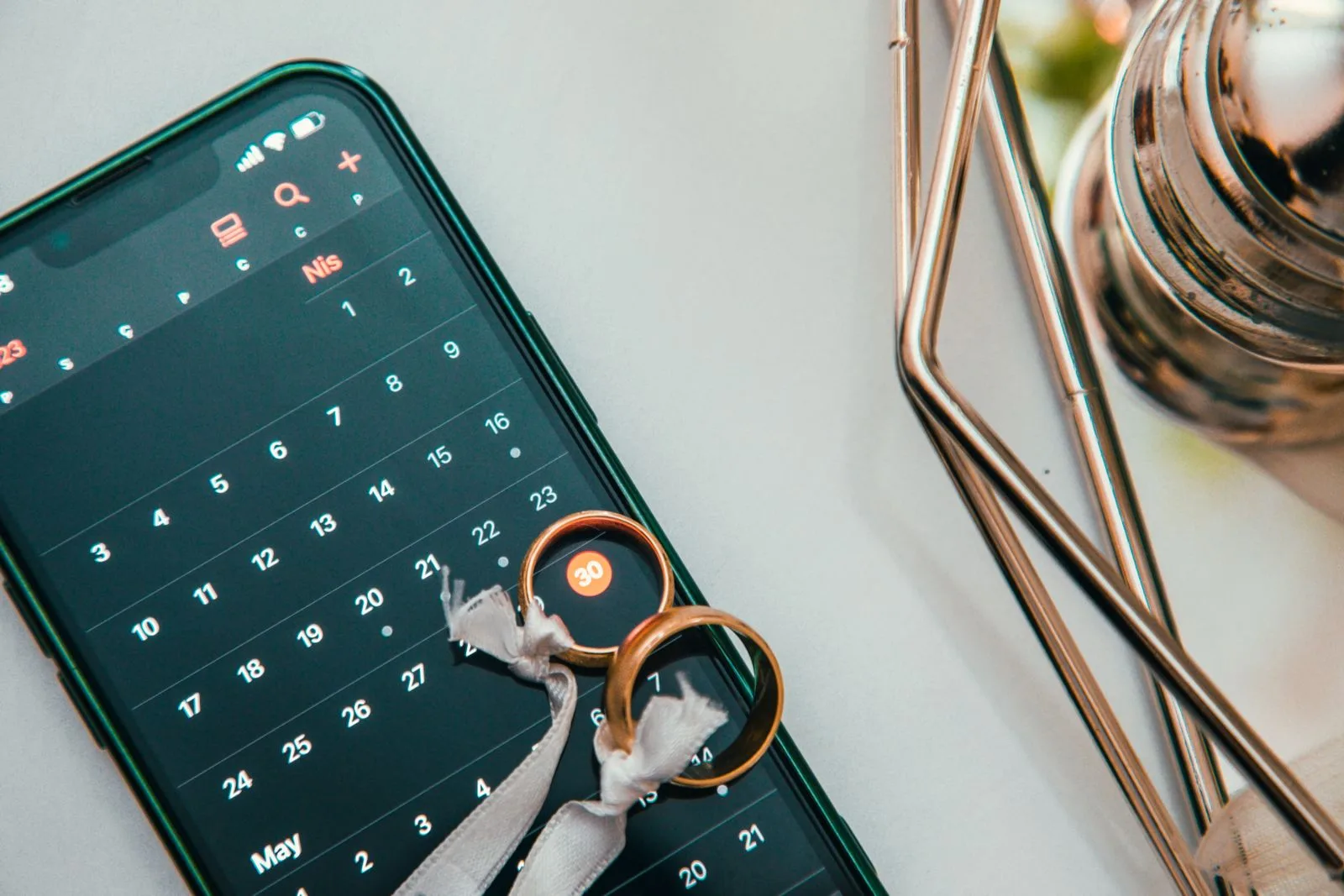 Two wedding rings resting on a phone calendar, for choosing a New York wedding date | Wedded Wonderland