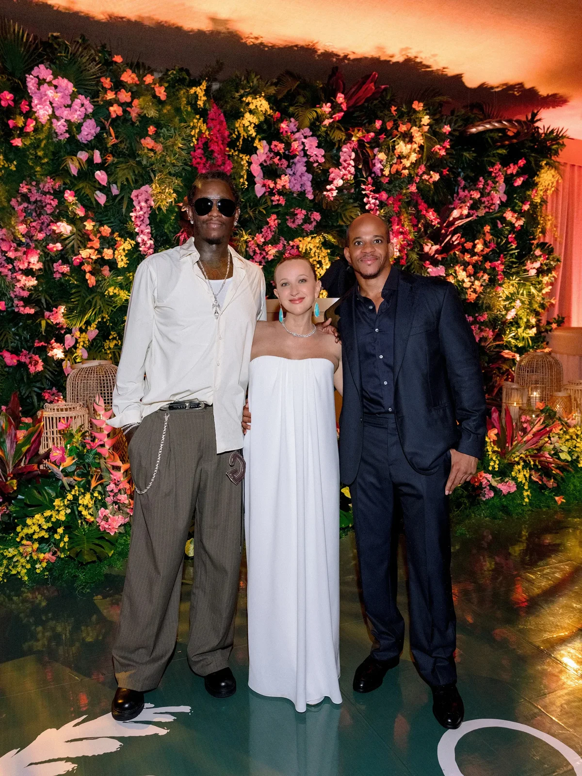 Jennifer Meyer in a white column dress in front of a wall of flowers at her wedding after-party | Wedded Wonderland
