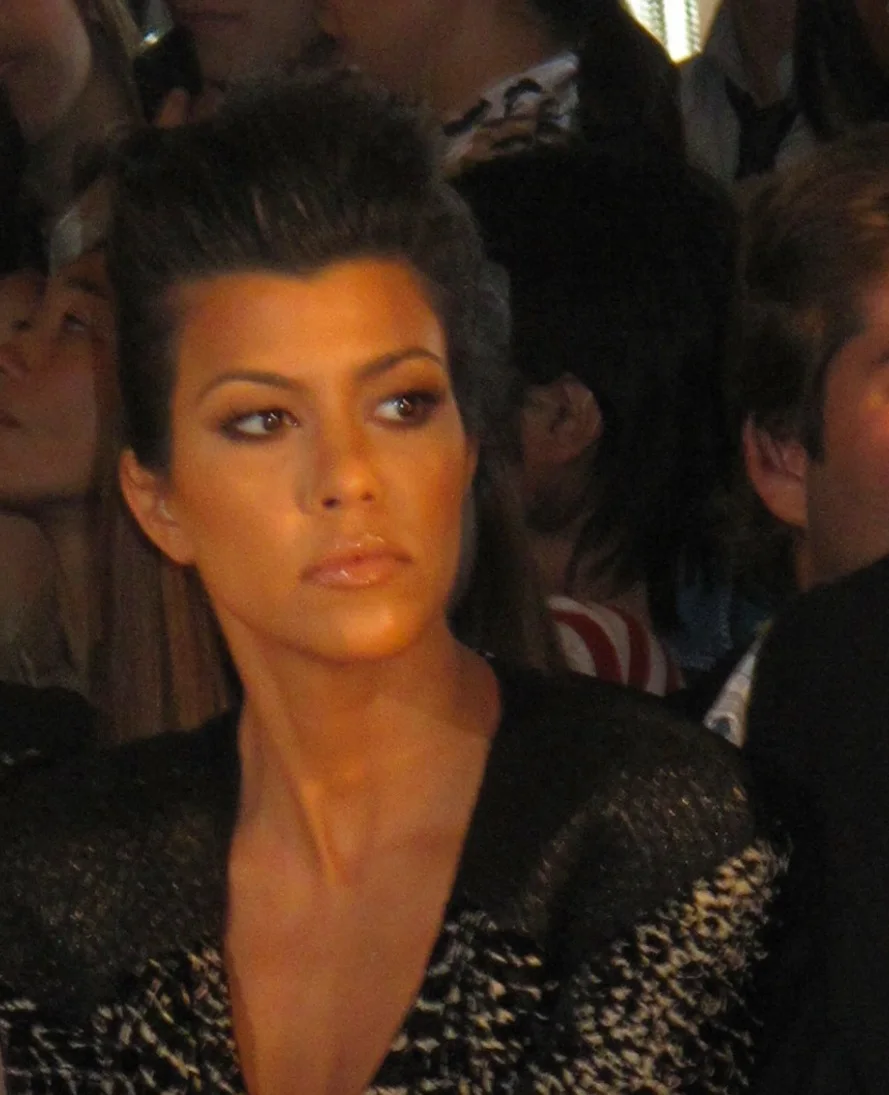 Kourtney Kardashian seated at a fashion event | Wedded Wonderland