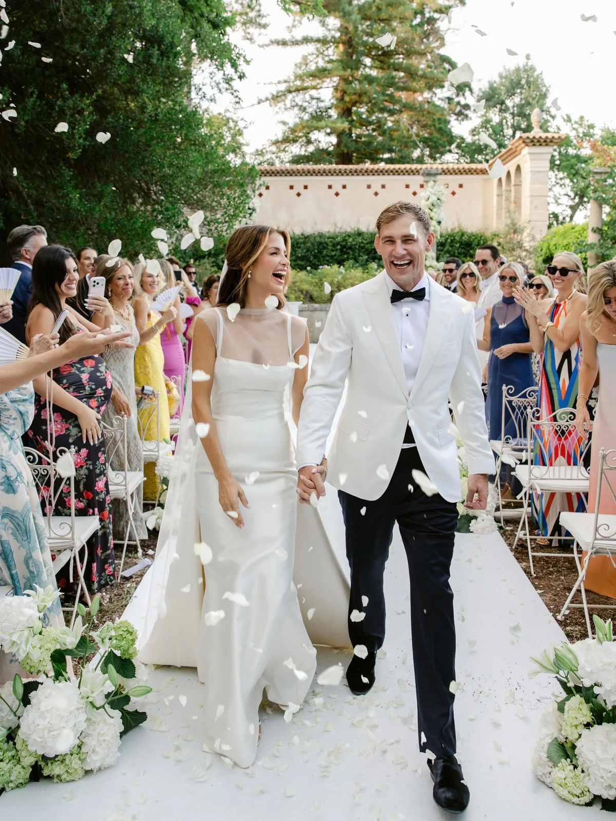 Naomie Olindo and Billy Haire walking back up the aisle under white rose petals at Château de Pradines | Wedded Wonderland