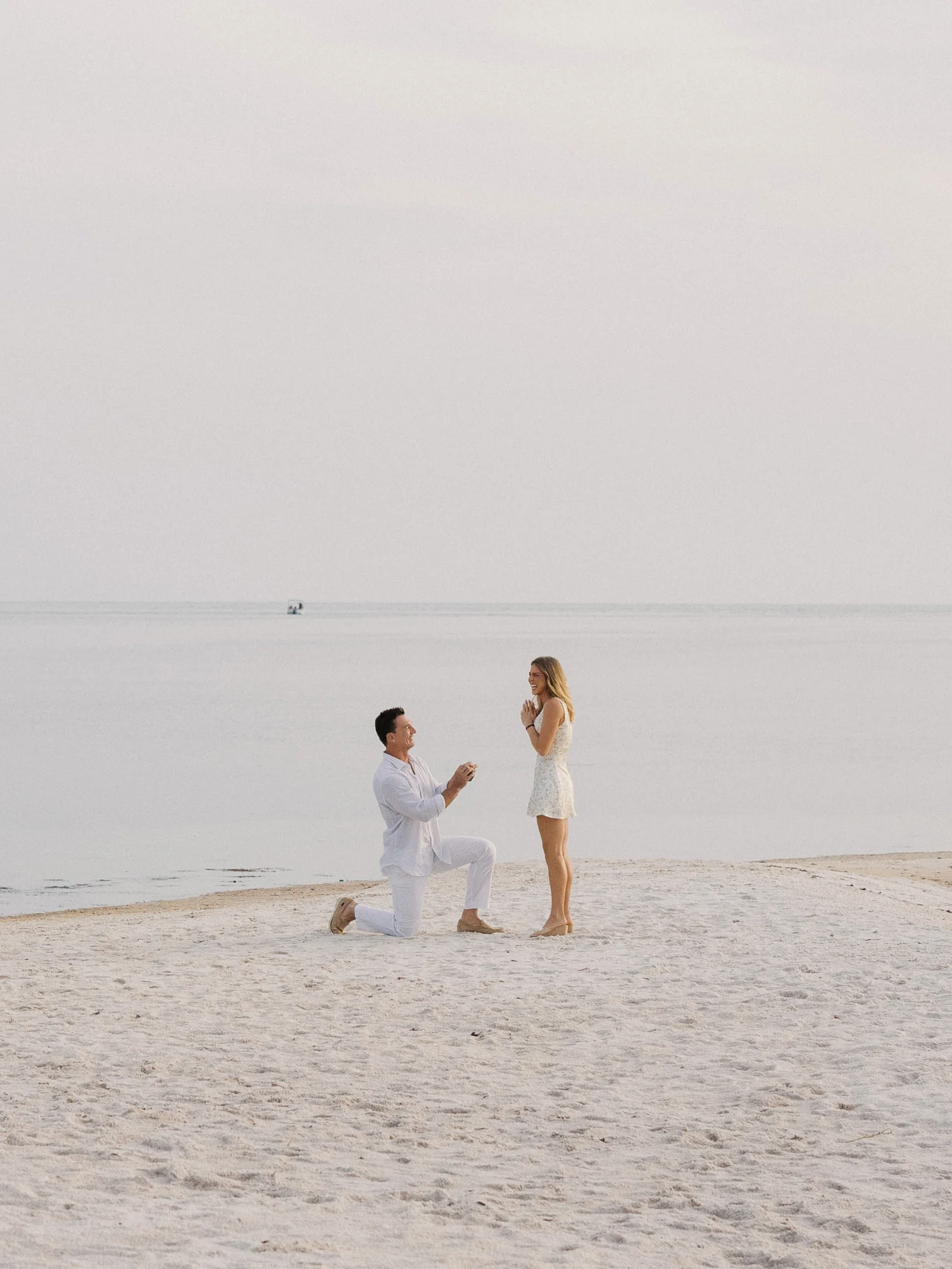 Tyler Cameron on one knee proposing to Tate Madden on a white sand beach | Wedded Wonderland